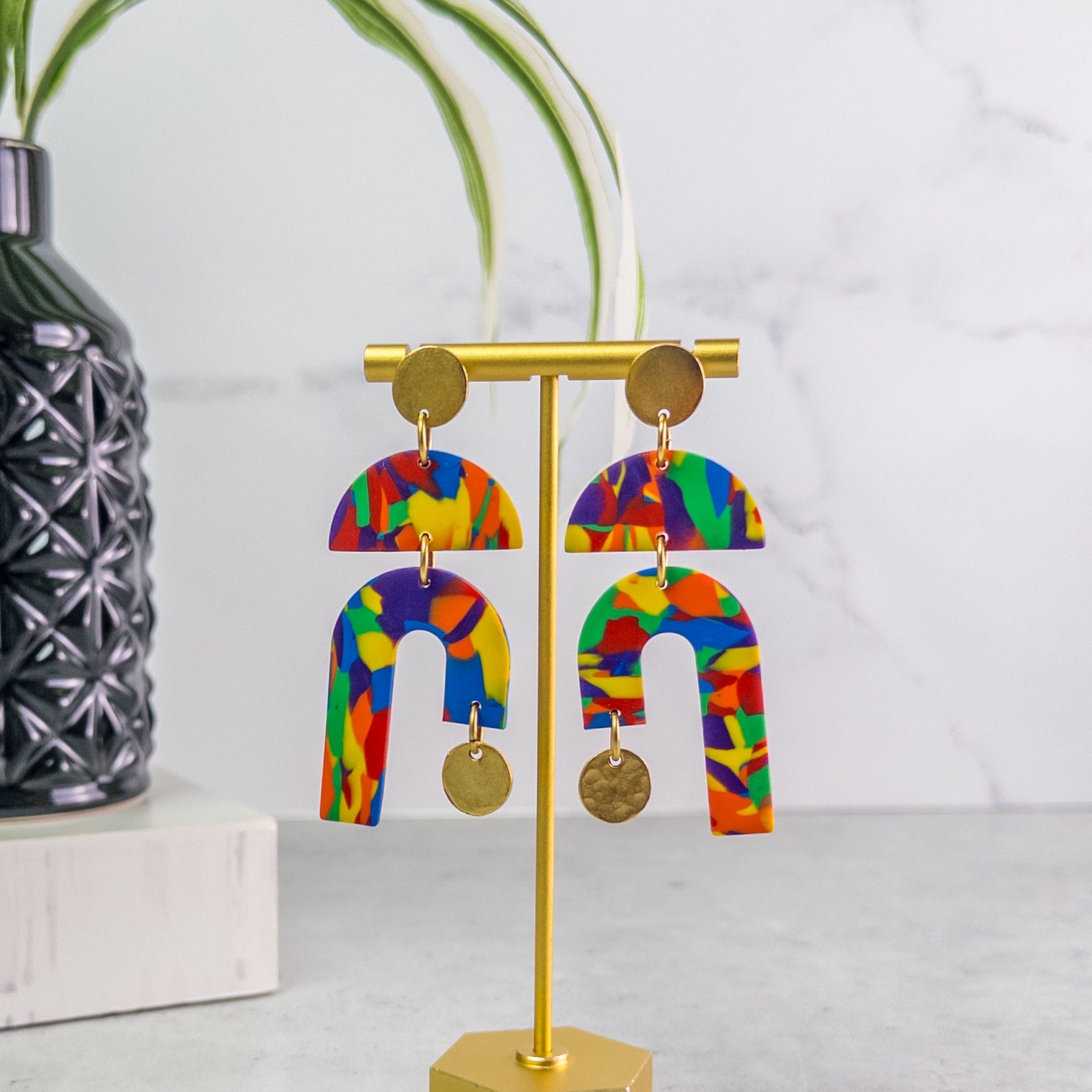 Colorful U-shaped pride earrings on a gold stand with a white background