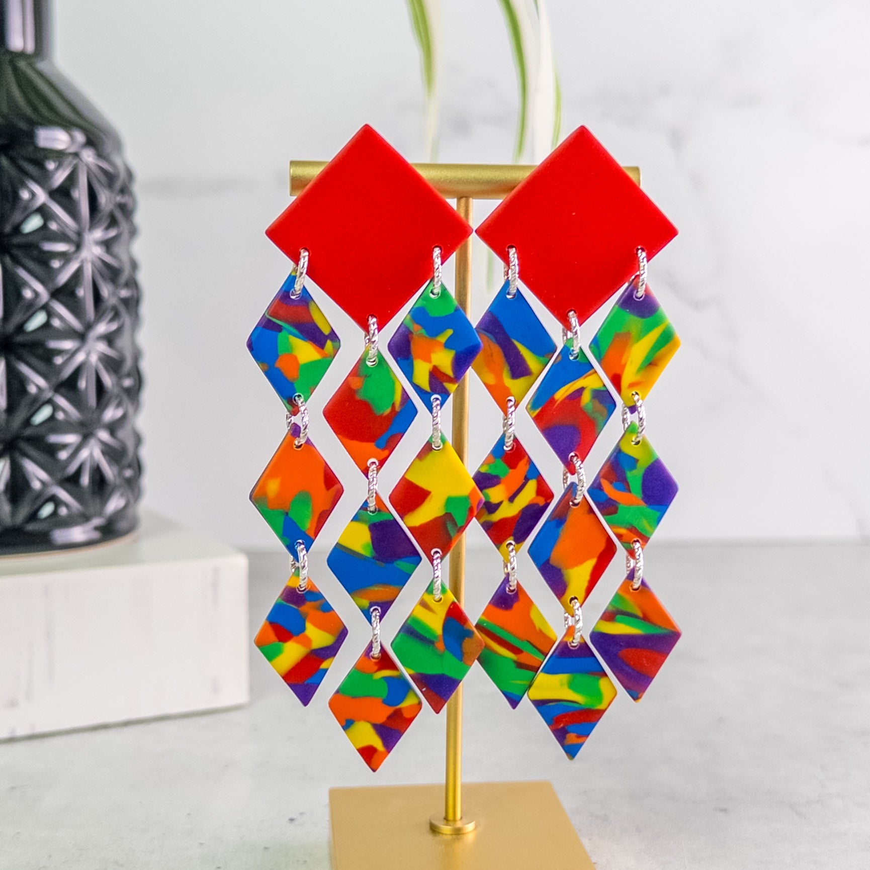 Colorful geometric pride earrings on a stand with a white background