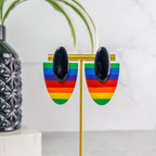 Rainbow pride heart-shaped earrings on a stand with a plant and vase in the background
