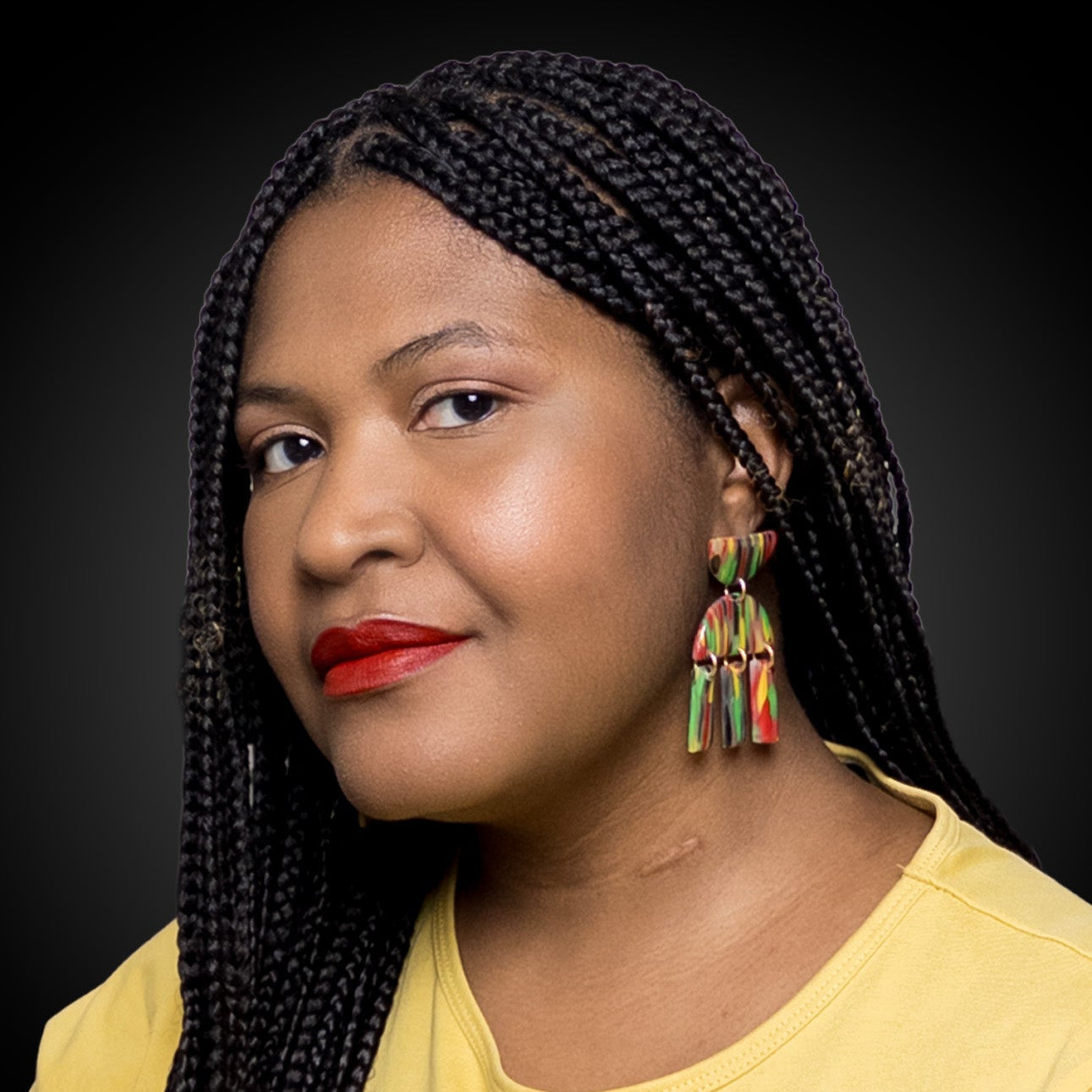 Woman with braided hair wearing black history month juneteenth black red green yellow abstract large statement dangle lightweight multicolored festive earrings