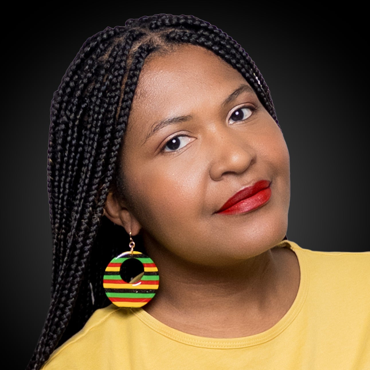 Woman wearing a yellow top and black history month juneteenth black red green yellow abstract large statement dangle lightweight multicolored festive hoop earrings