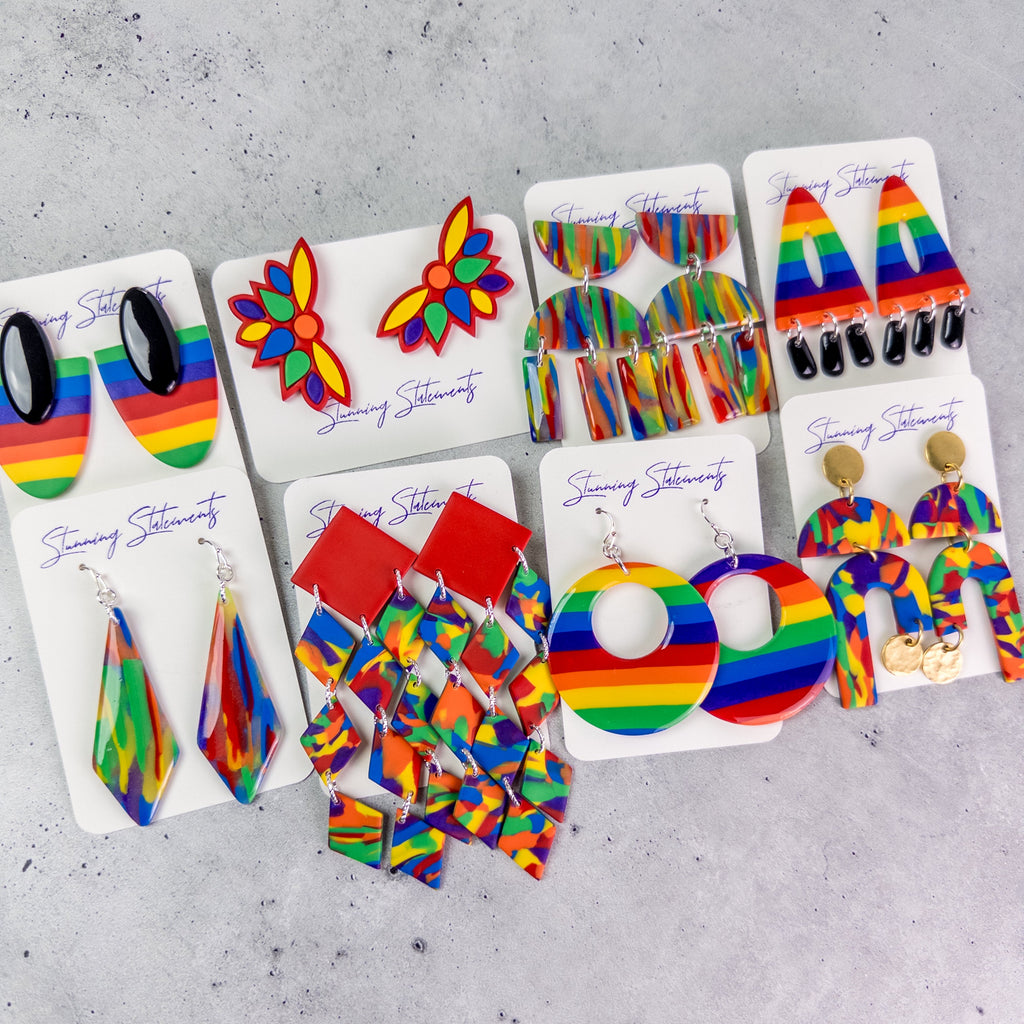 Colorful pride month earrings on display cards against a gray background