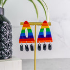 Rainbow pride  triangle earrings on a gold stand with a plant and vase in the background