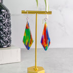 Colorful teardrop pride earrings on a gold stand with a white background