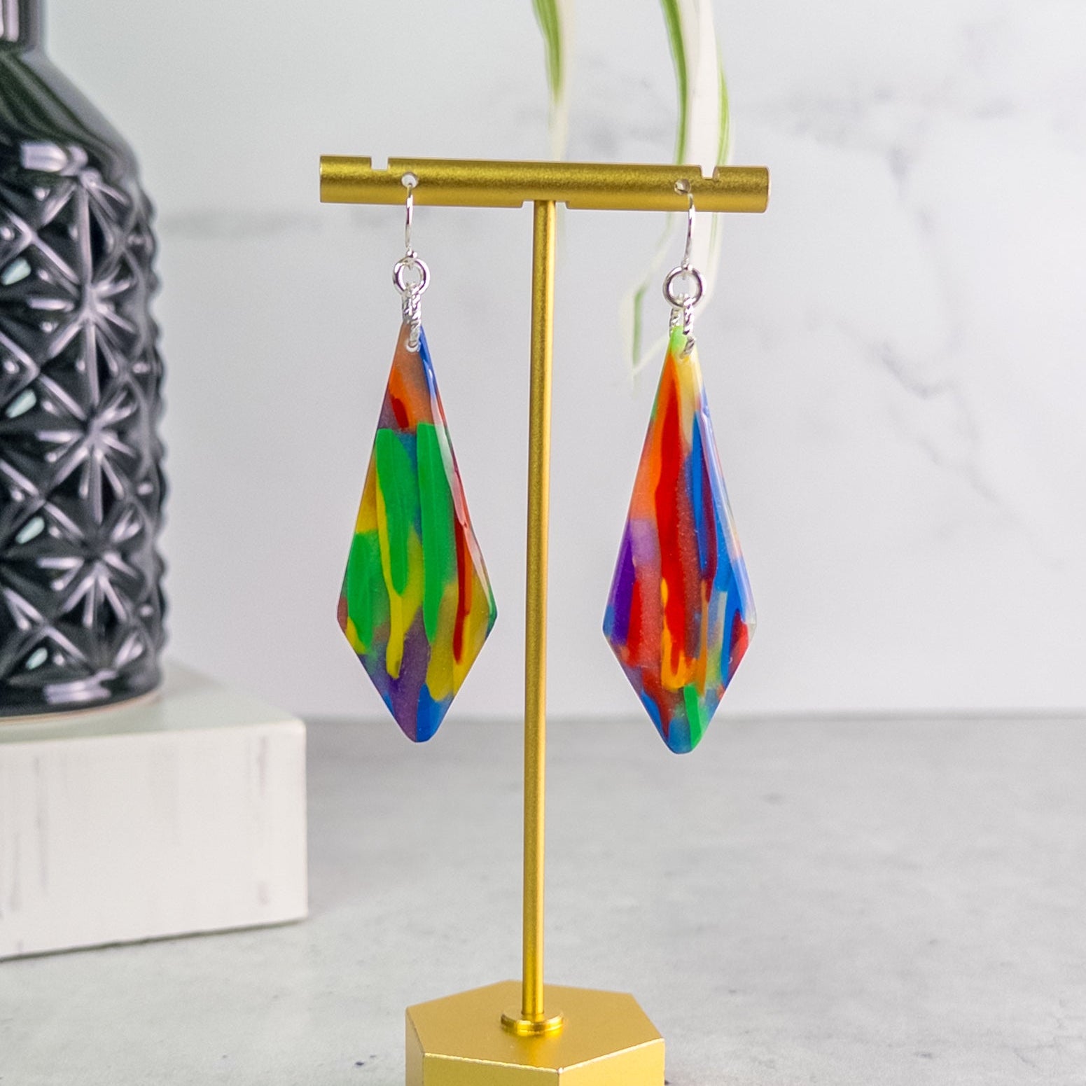 Colorful teardrop pride earrings on a gold stand with a white background